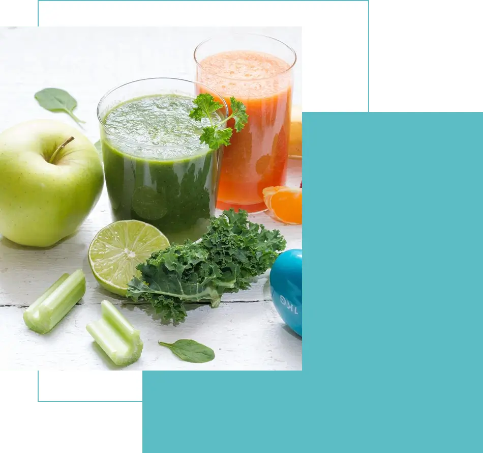 Green and orange vegetable juices with fresh produce on a white surface.